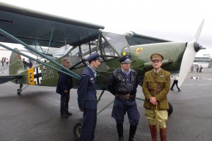 Pilots pose in front of a mono-wing WWI fighter plane